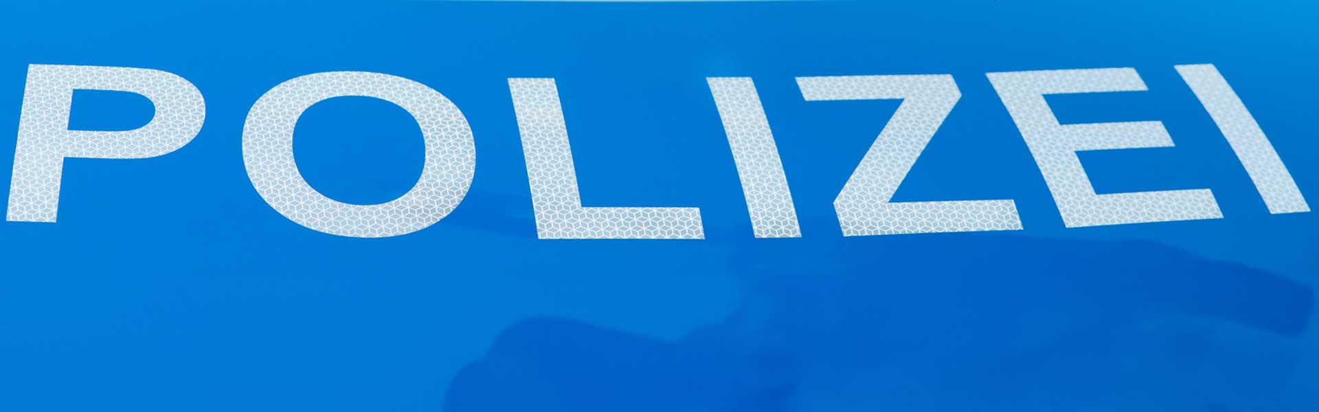 Arm der eine "HALT POLIZEI" Kelle hält mit Polizeischriftzug im Hintergrund