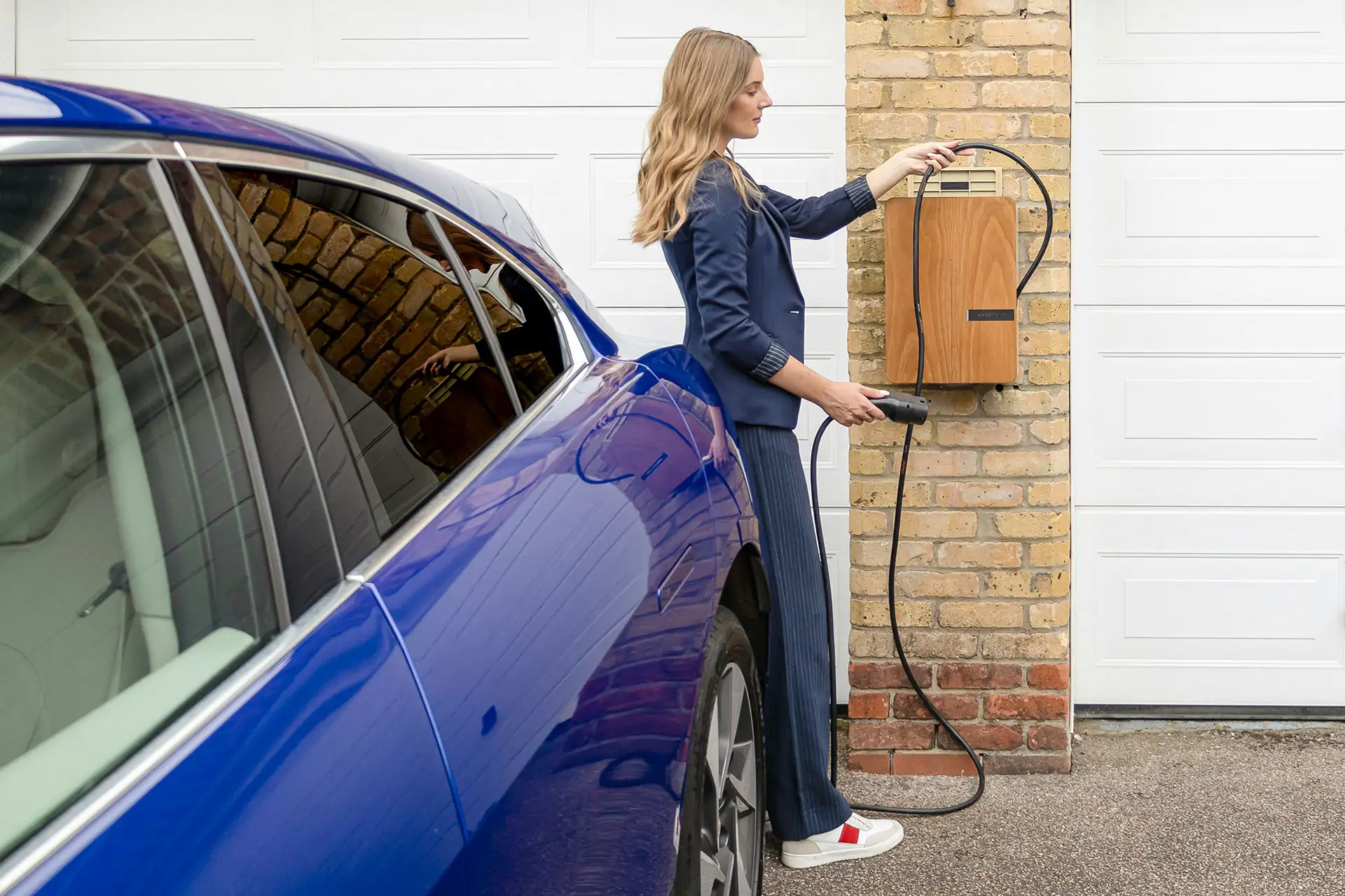 Eine Wallbox ist im Vergleich zur Haushaltssteckdose auf die höhere Belastung ausgelegt, die beim Laden des Batteriespeichers im E-Auto auftritt. Eine Frau steckt ihr E-Auto an einer Wallbox an