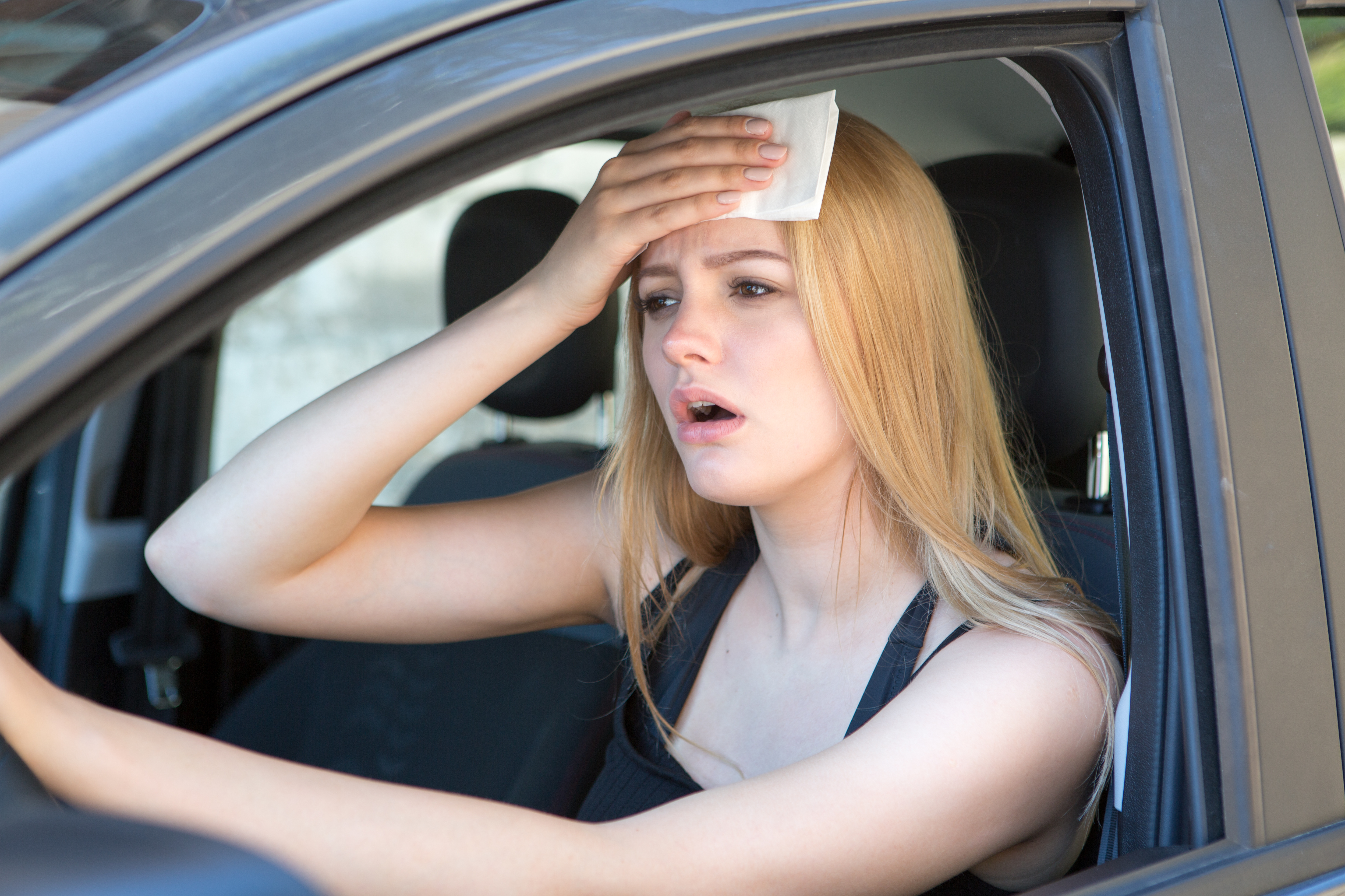 Frau schwitzt im Auto bei heißen Temperaturen